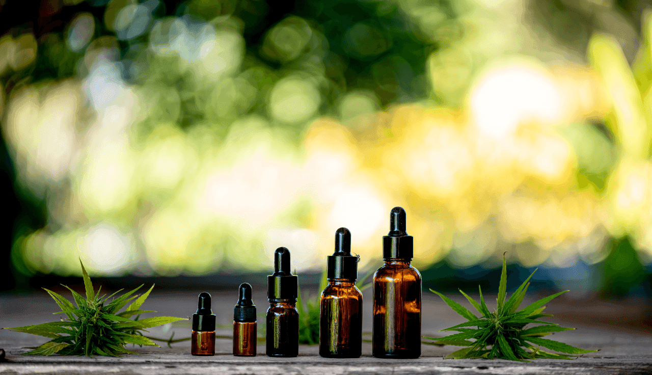 Pipetten-Flaschen in verschiedenen Größen. Daneben Cannabis-Blüten.